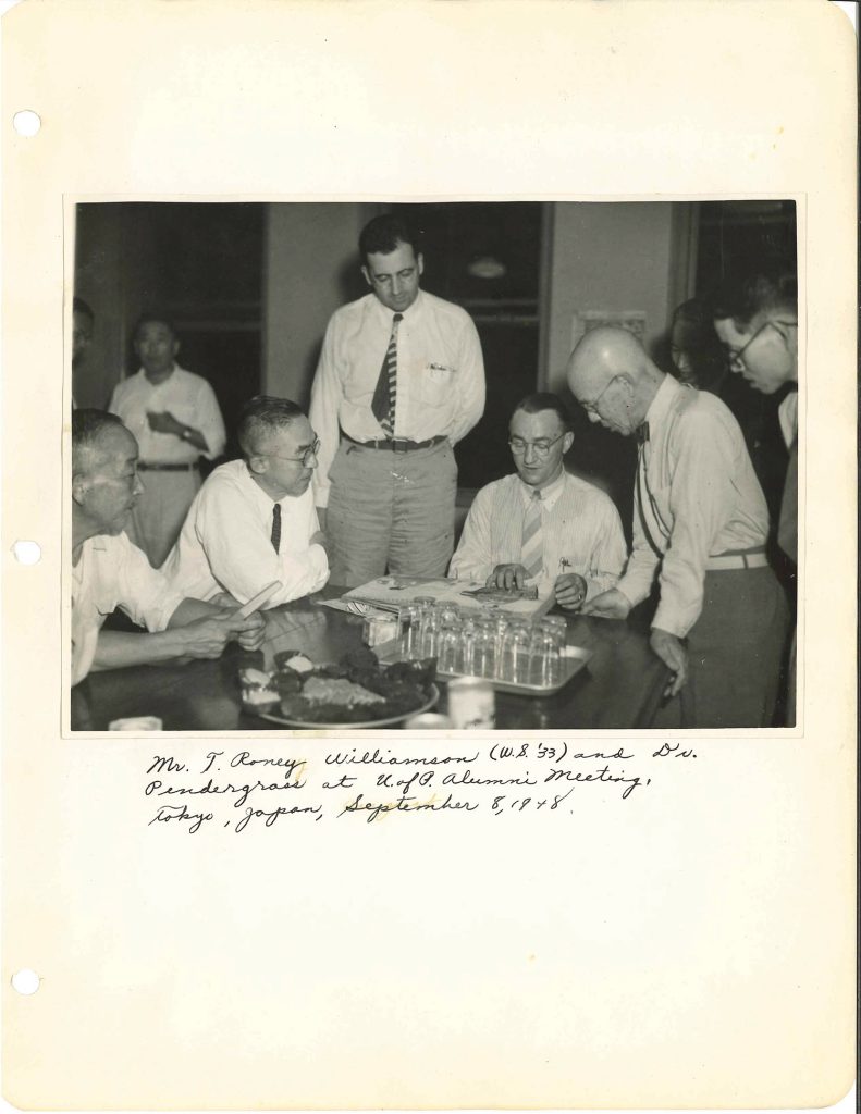 An image of a scrapbook that includes a black and white photograph of four men looking at an album on a table in the foreground with handwritten text underneath.