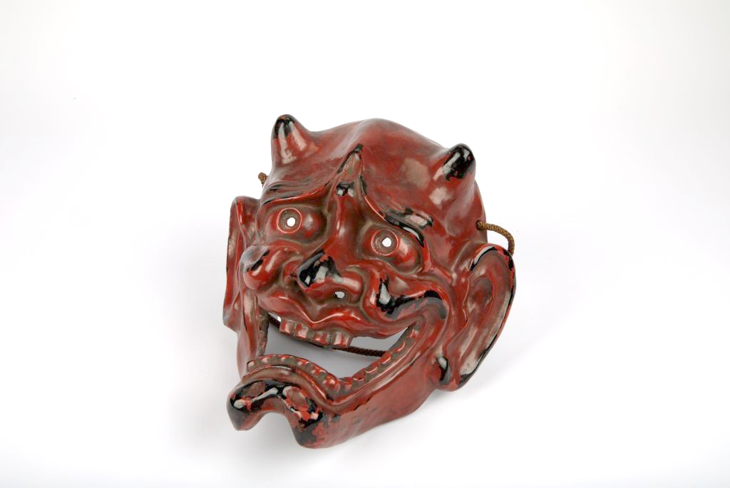 Picture of a red demon face mask with small horns and a wide open grin 